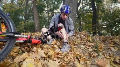 一个年轻人从一辆自行车上摔下来后坐在公园里，缓解膝盖的疼痛，在公园里骑一辆危险的自行车